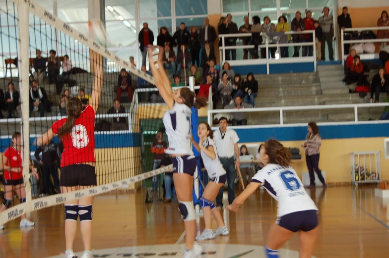 girls are playing volleyball inside the gym while people watch