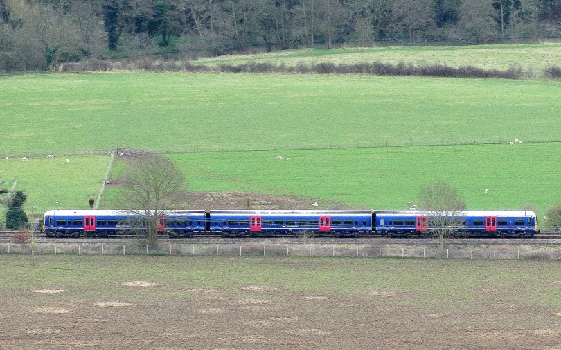 a blue train with many cars traveling along the tracks