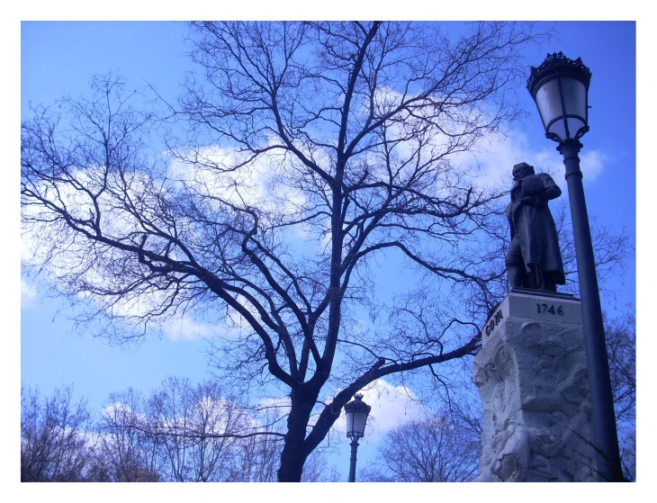 an old fashioned lamp post next to a large bare tree