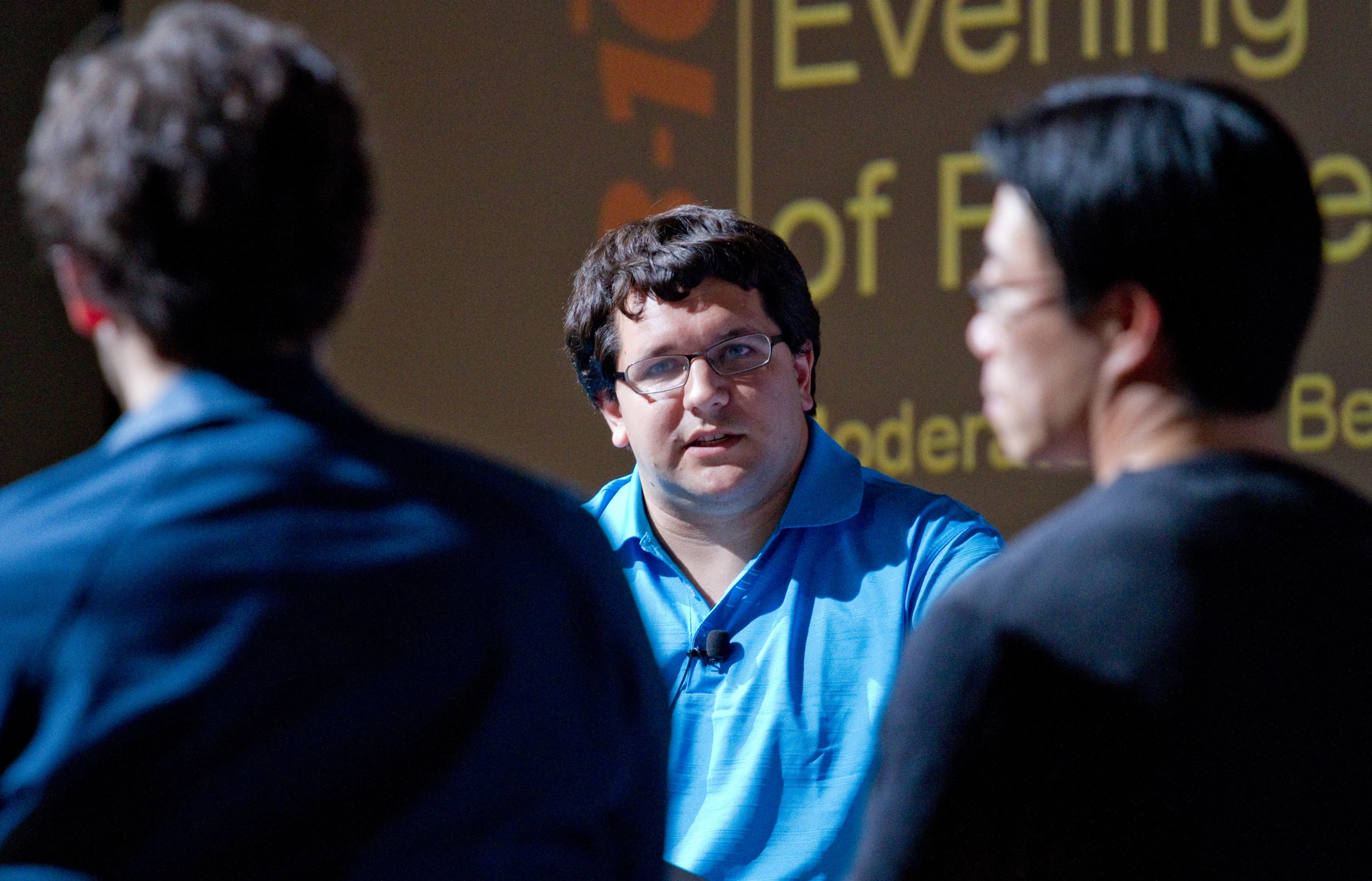 two men talk at a gathering in front of a crowd