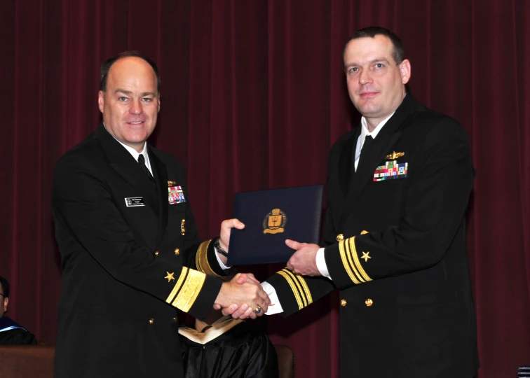 two men in military uniforms shaking hands while wearing dress uniform