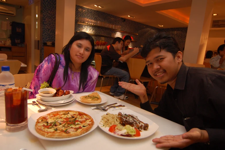 two asian people smiling and eating pizza at the same time