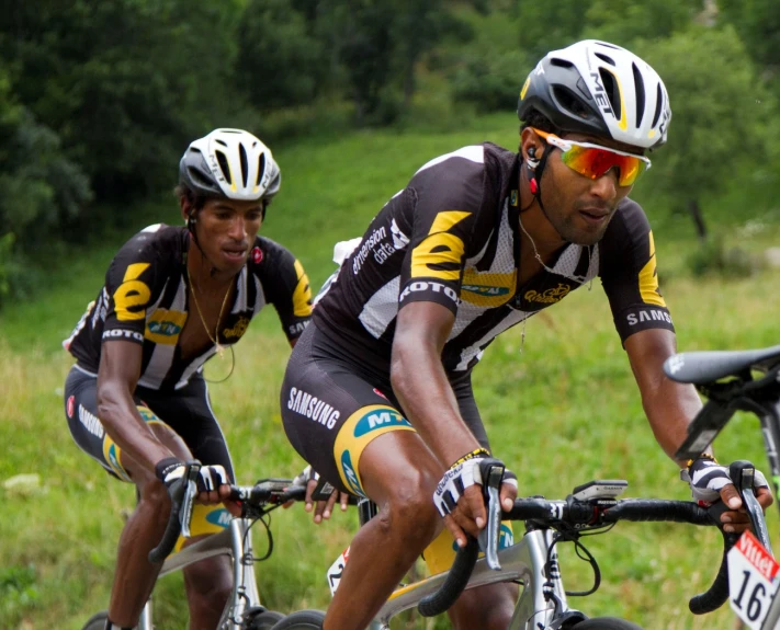 two men riding bikes through the grass in a rural area