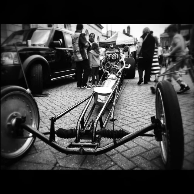 a car motorcycle sits parked on the sidewalk with people near by