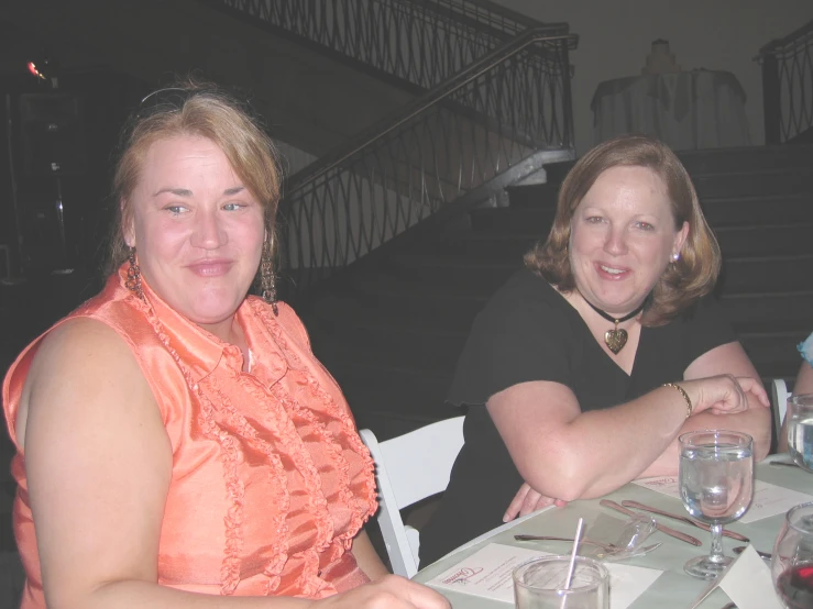 two women at a table together in front of some stairs