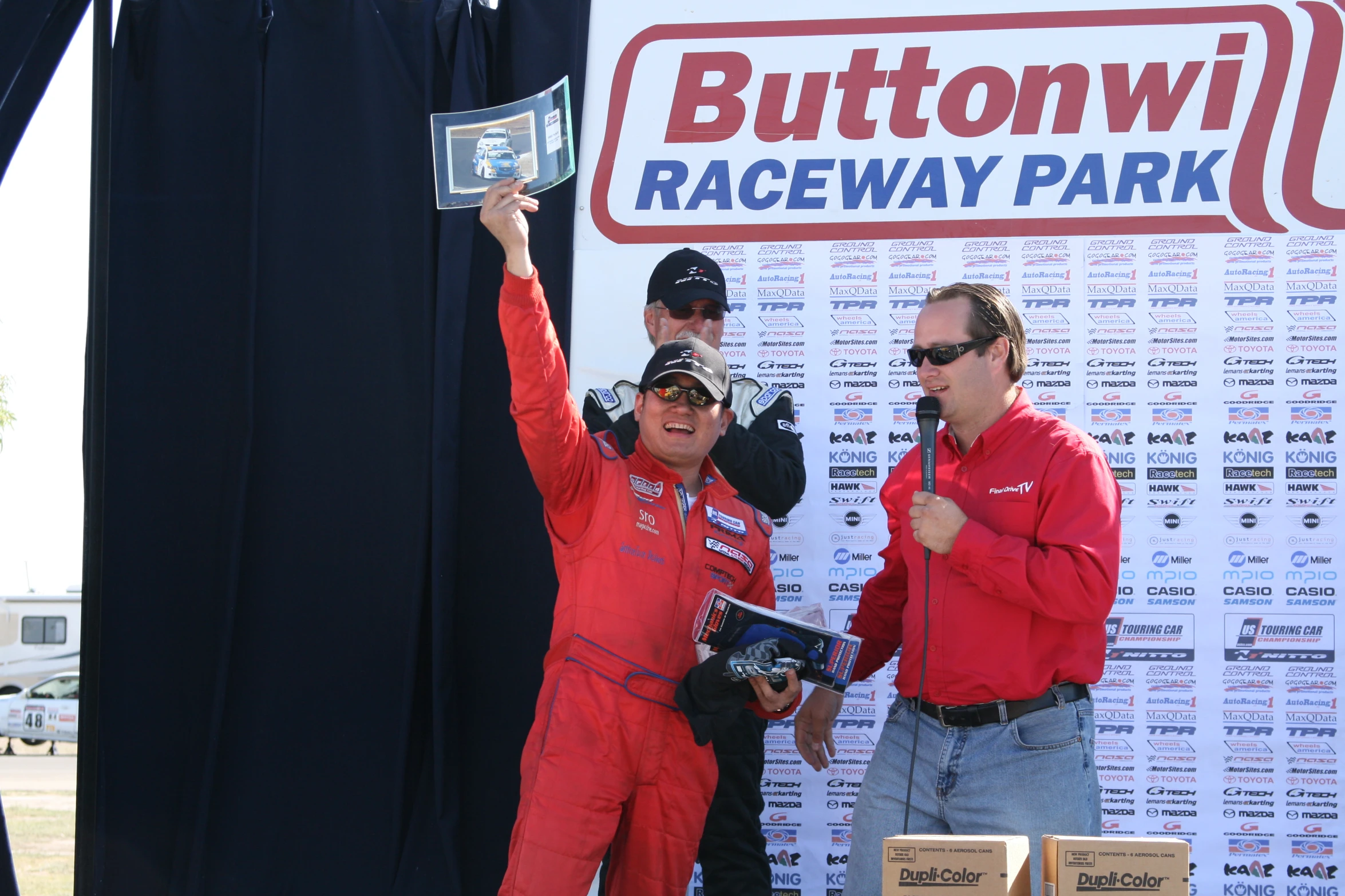 two men in racing gear on stage with a sign