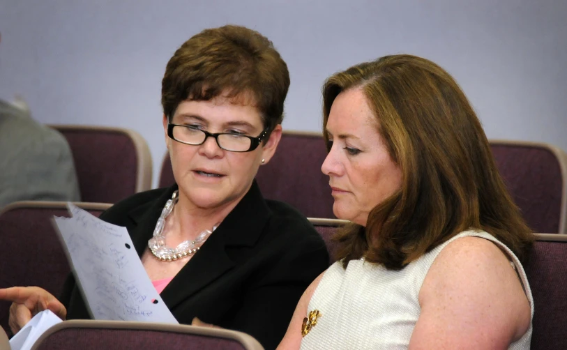 two women sitting in chairs looking at paper