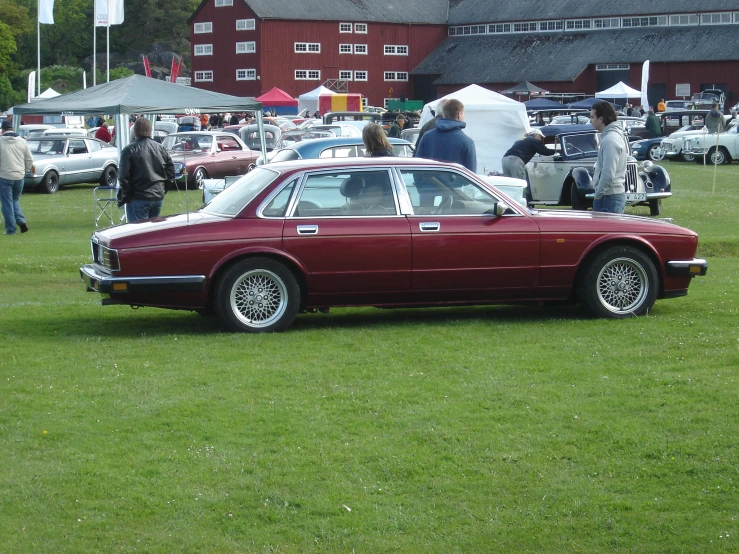 an antique maroon car sitting on top of a lush green field