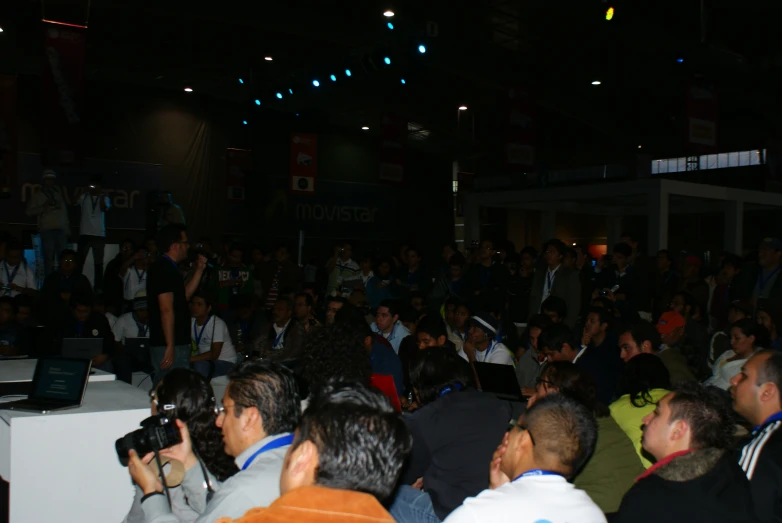 a crowd of people sitting in front of a man on a laptop computer