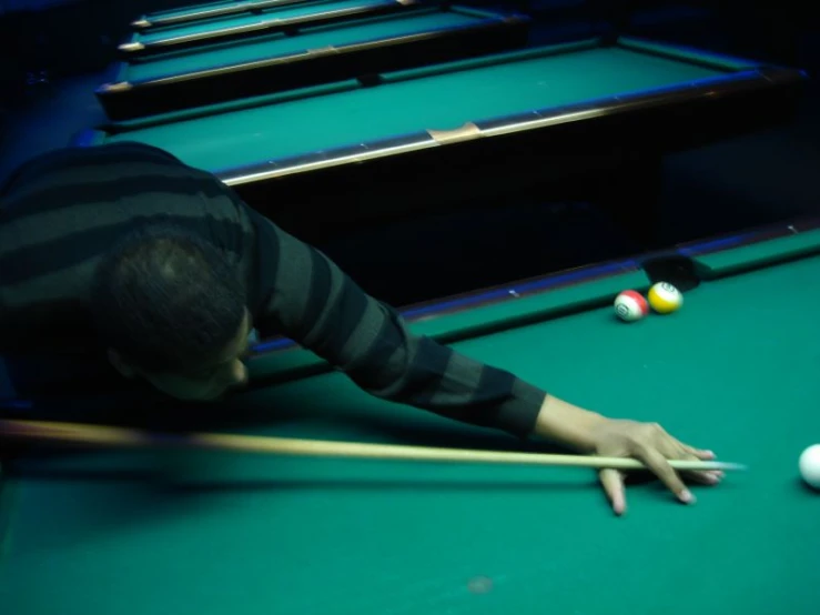 a man bent over playing pool in a dark room