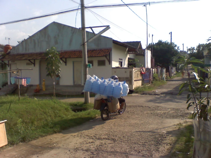 an old man rides a moped with three bags of water on the back