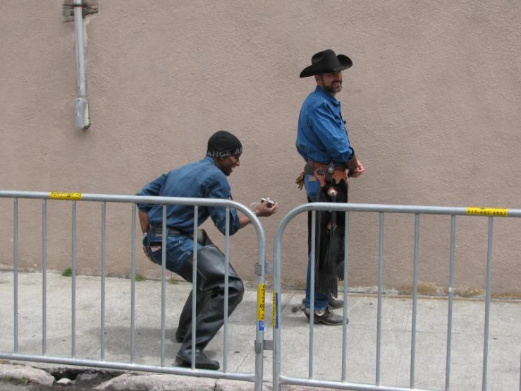 two men with cowboy hats climbing over barricades
