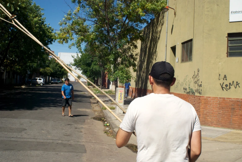 a man holding a wooden stick on a street next to a person