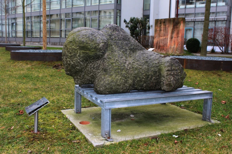 a sculpture on top of a metal bench on grass in front of buildings