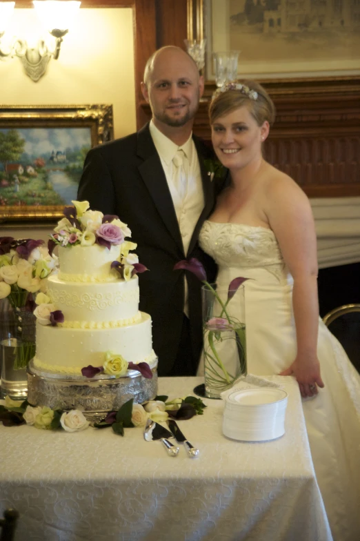 two people stand next to a wedding cake