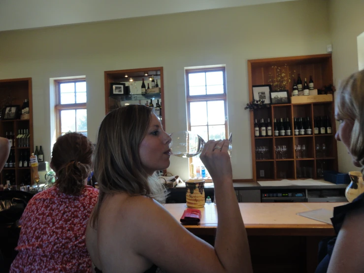 a woman standing in front of two other women holding wine glasses