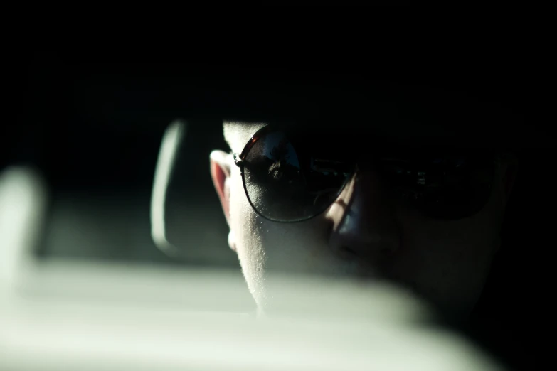 a man wearing shades sitting in a car looking at his phone