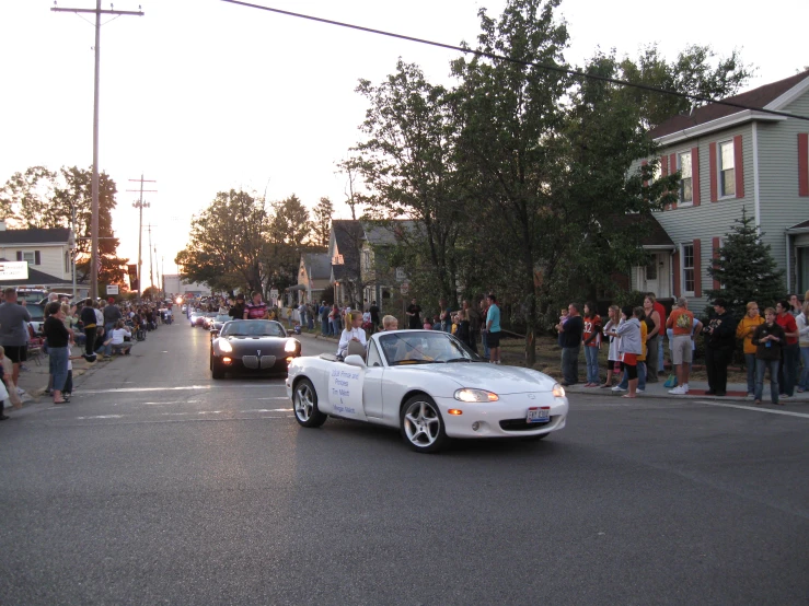 a white sports car driving past a crowd of people