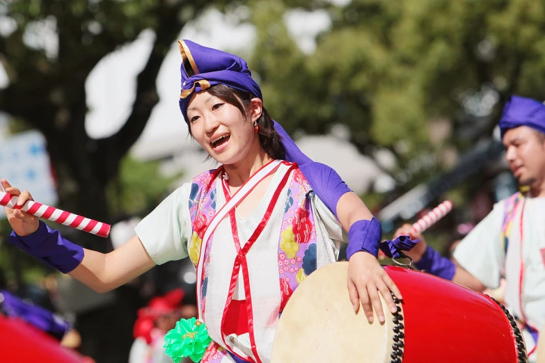 a woman wearing blue is playing a tamba and looking at the camera