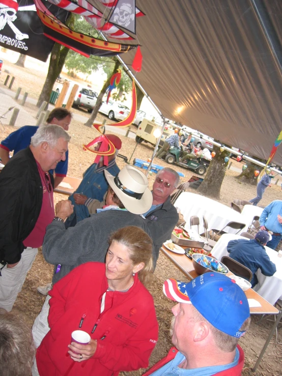 several people standing under umbrellas and tables eating