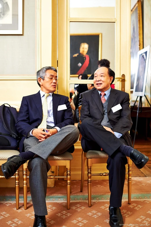 two men in suits sitting down and one man sitting down on chair