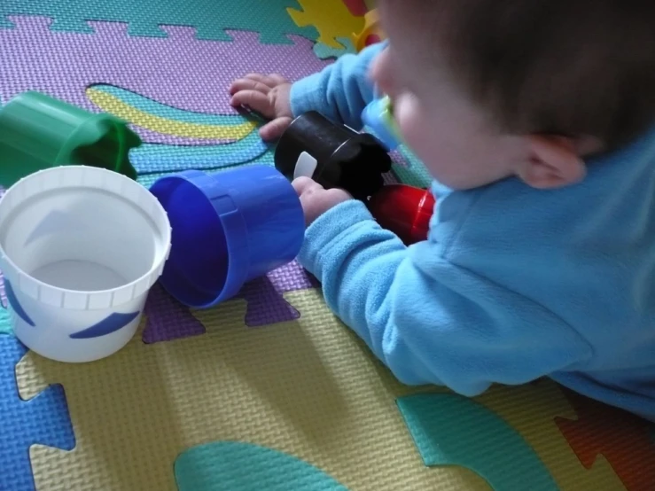 baby laying on a colorful blanket and holding cups