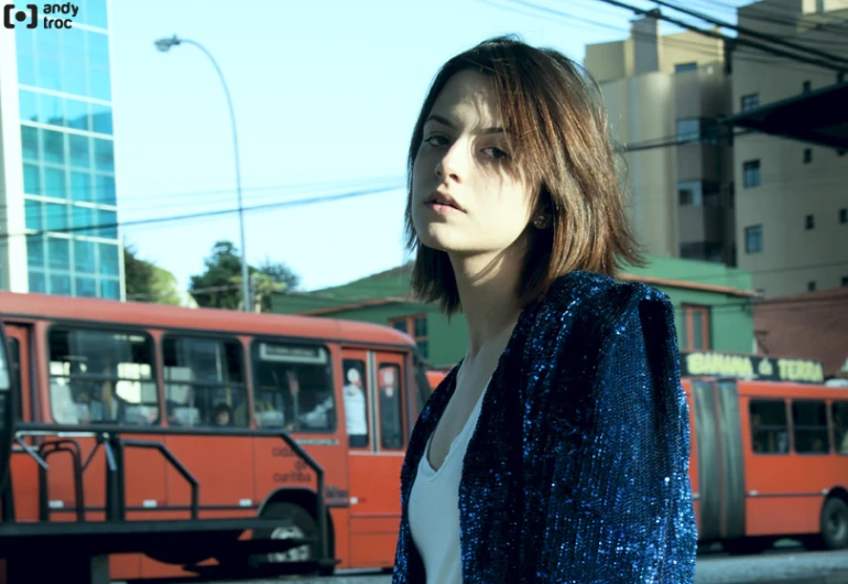 the woman stands on the side walk in front of an older red bus