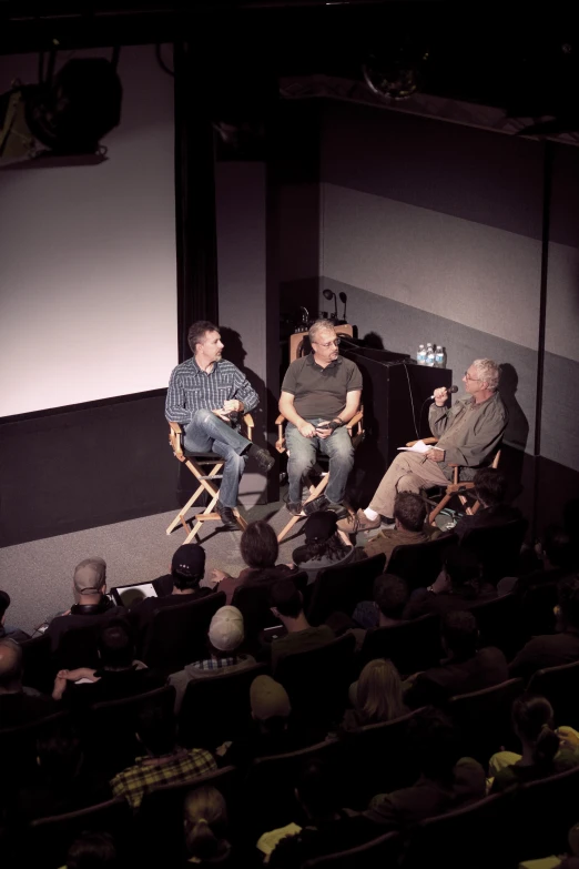 three men are sitting in chairs and a guy is standing