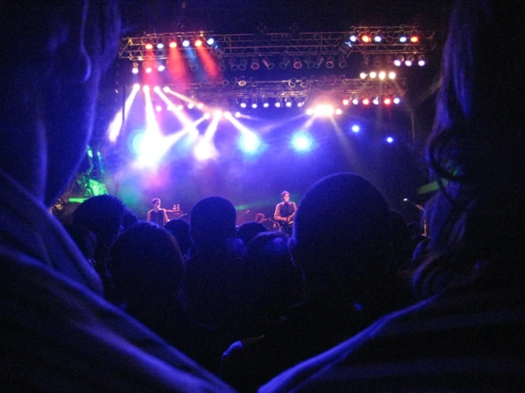 many people are sitting at the edge of a stage, and bright lights shine through