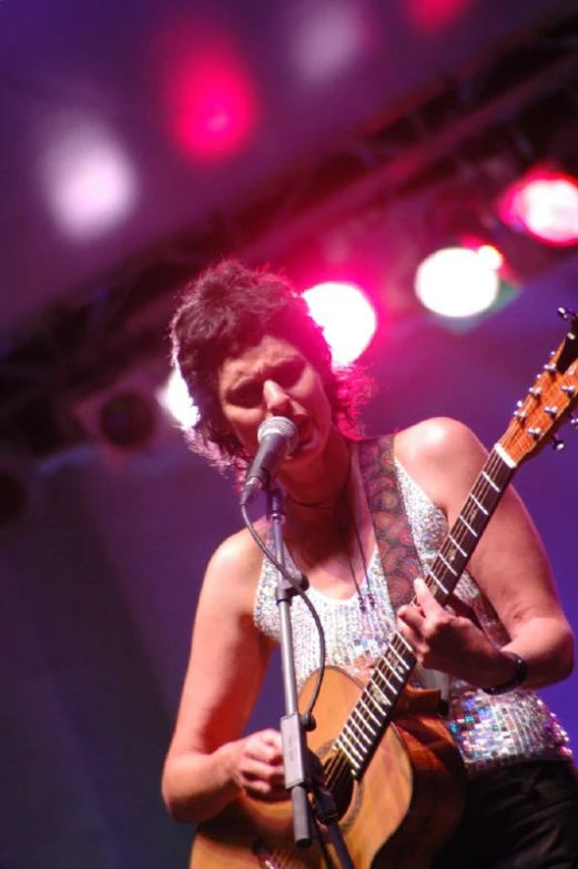 a female guitarist in white singing on stage with bright lights