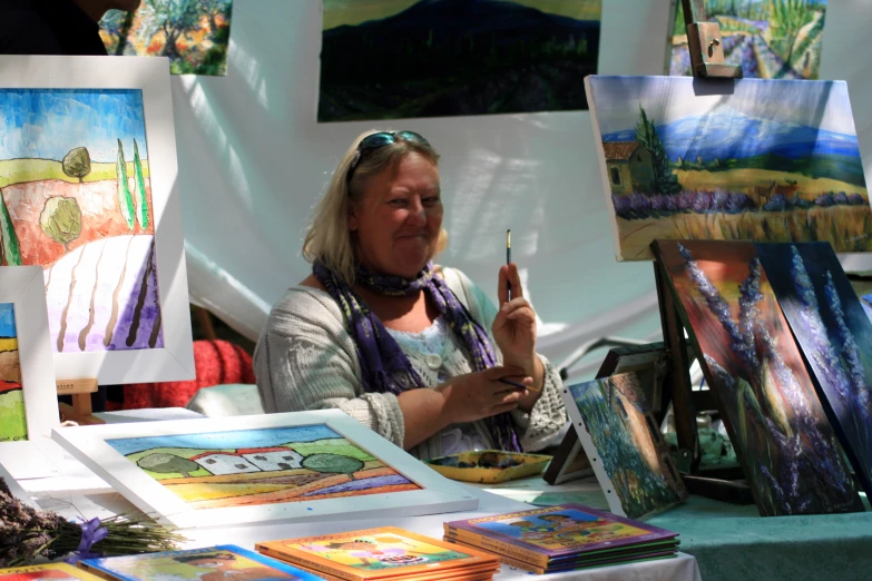 a woman at an art stand smiling and holding a pen