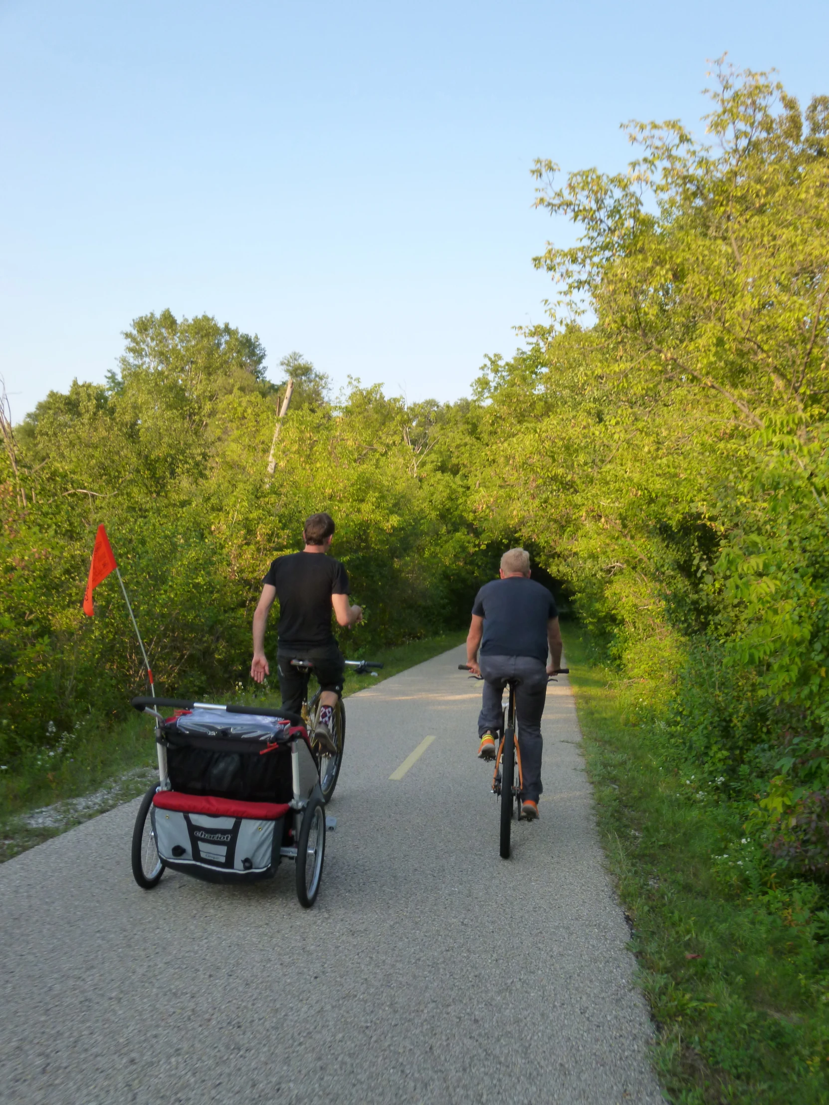 two people riding bikes on a path next to a forest