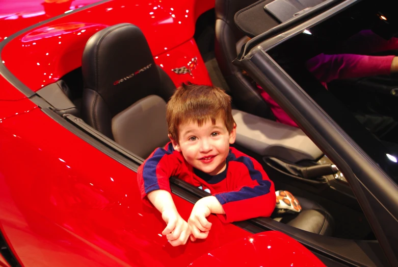 a small boy sitting in the top of a red sports car