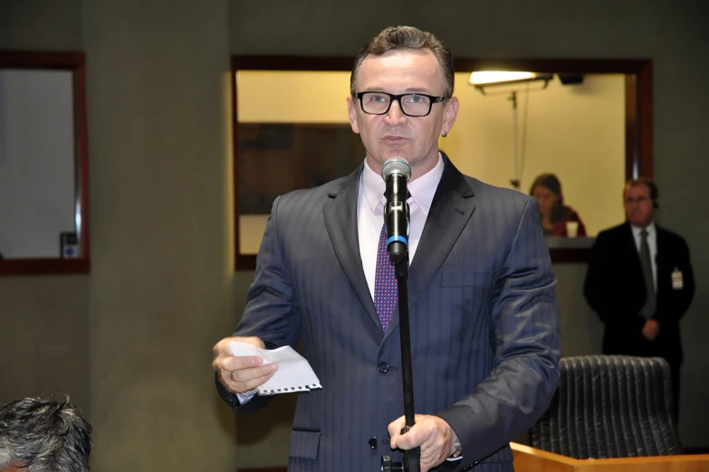 a man speaking with a microphone and papers in hand