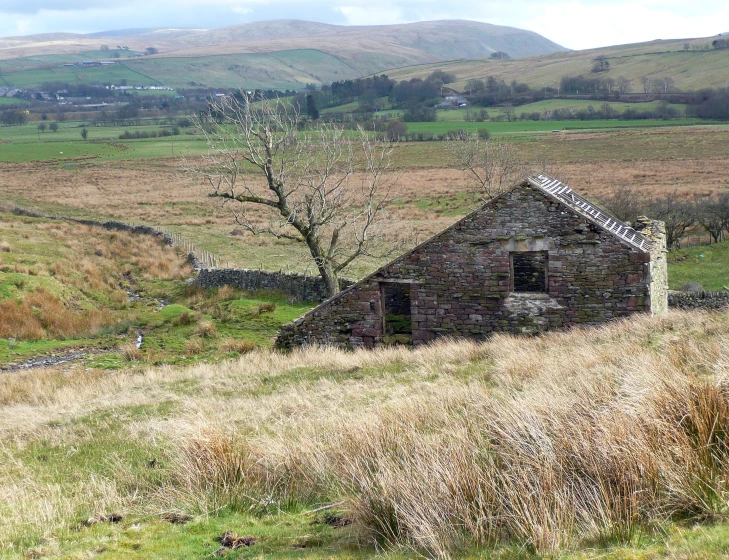 an old stone building in the middle of a grassy field