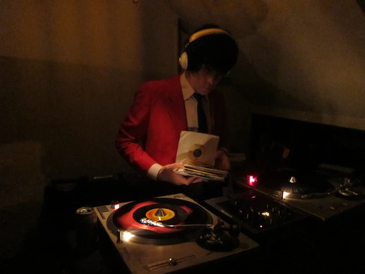 a man in red jacket standing next to djs decks