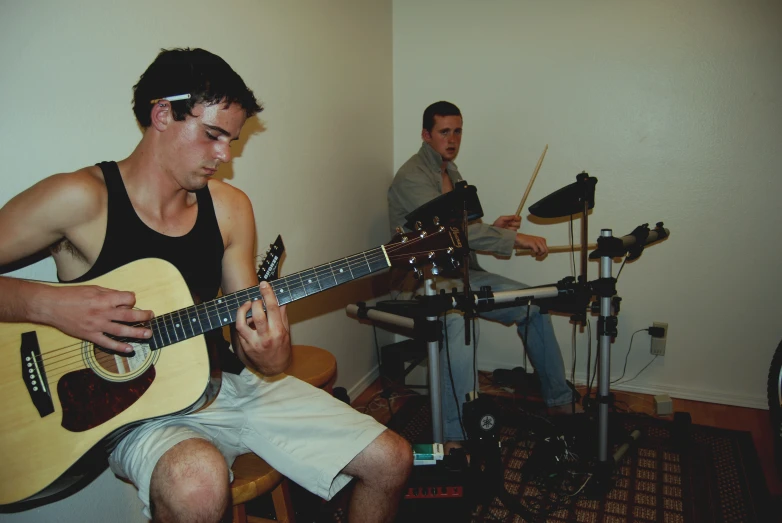 a male playing an acoustic guitar with a man in the background