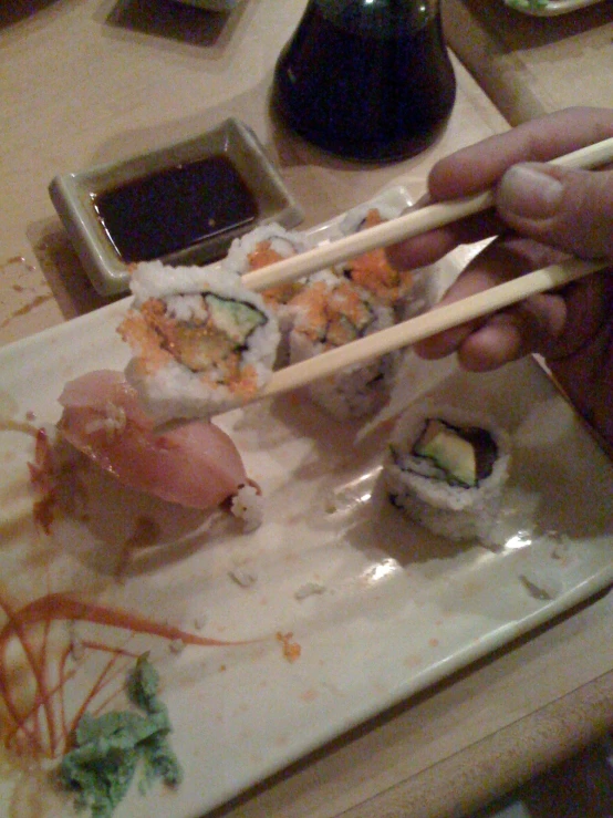 a hand with chop sticks holding sushi on the table