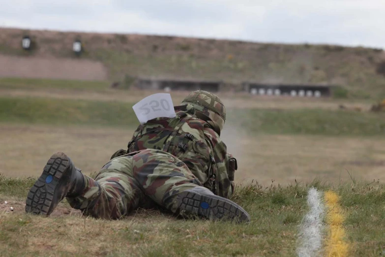 a military man in camouflage laying on the ground with his feet crossed