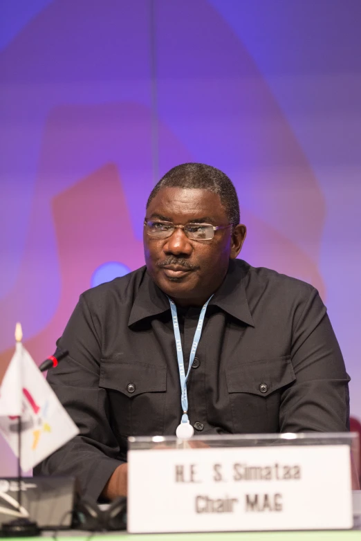 a man with glasses sitting at a table in front of a microphone