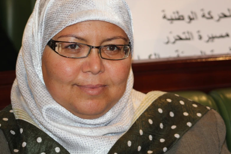 a woman with glasses in front of a white sign