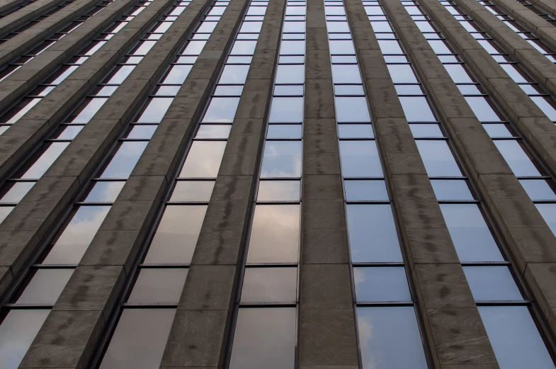 a very tall building has its windows reflecting the sky