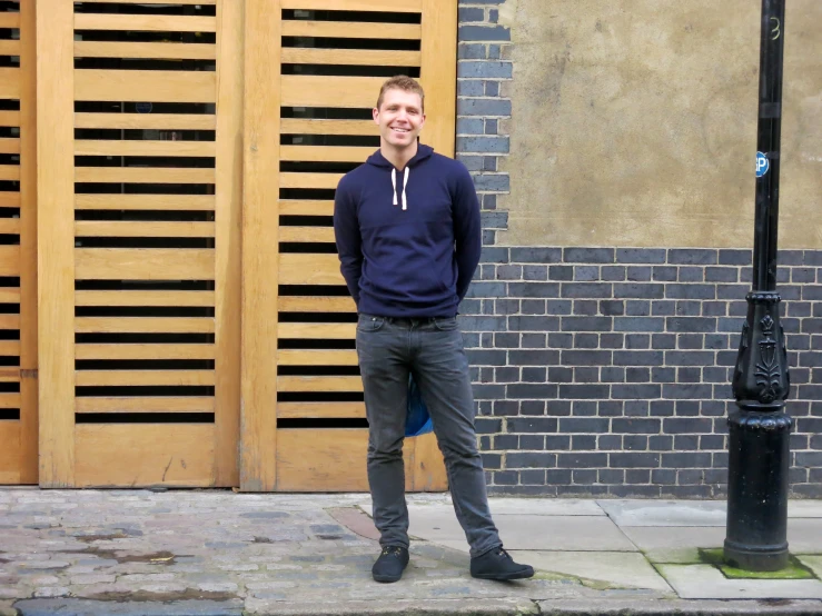 a man with a black sweater standing in front of a fence