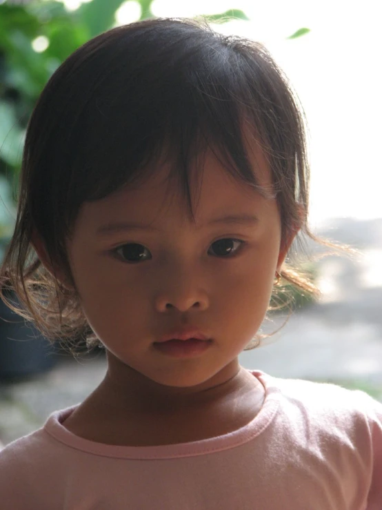 a young child wearing a pink shirt, with a small tree in the background