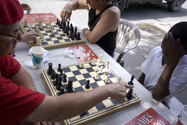 three men are playing chess in front of a red sign