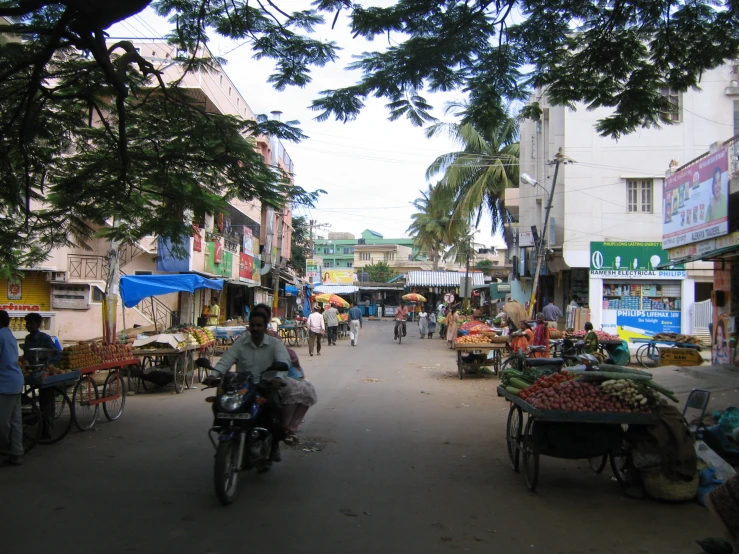 a man on a motorcycle rides through an outside market