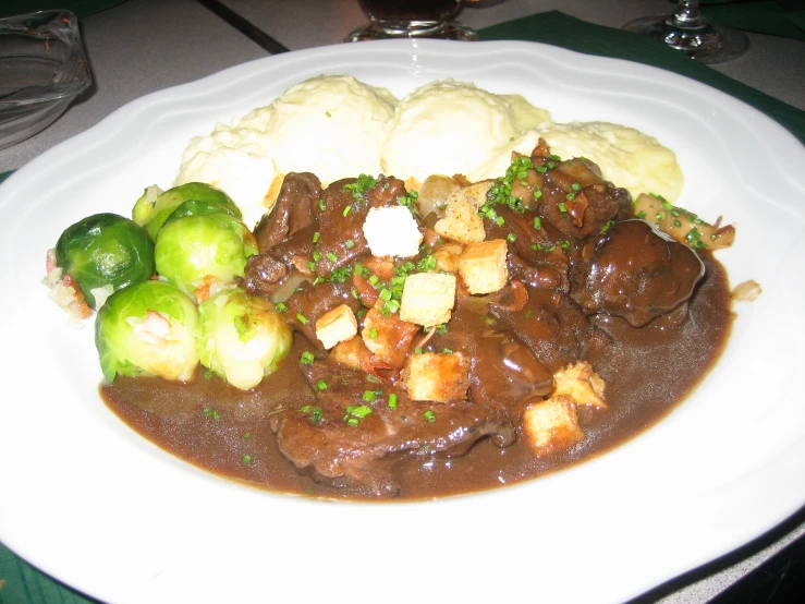 a plate of meat and potatoes covered in sauce with gravy