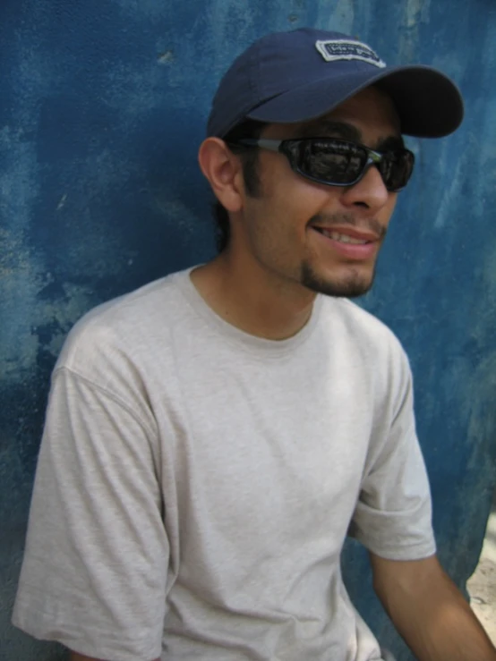 a man sitting against a blue wall and wearing sunglasses