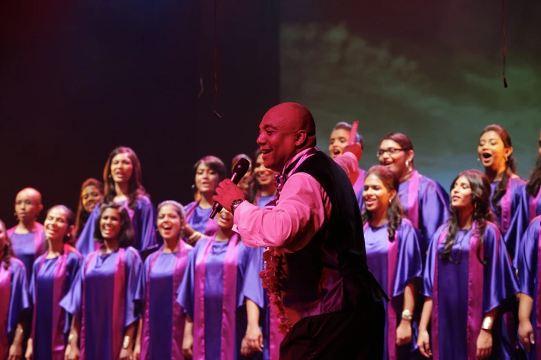 a male singer standing with his arms folded in front of a large group