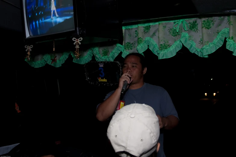 a man on stage with a mic, lighting and a large television